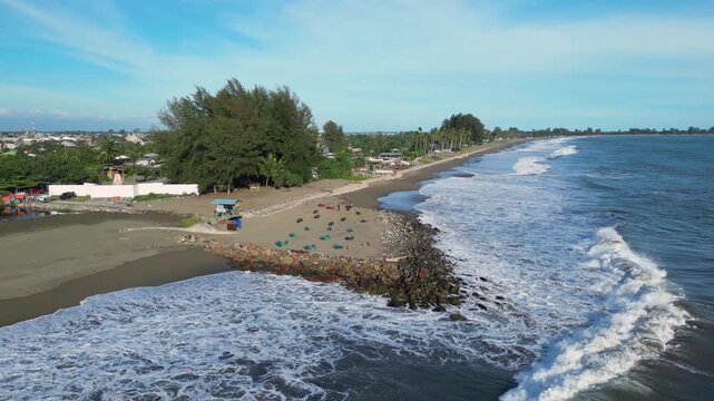 Meulaboh, Indonesia : Orbit aerial drone footage of wave breaks into beach by small stalls in Meulaboh, coastal town in Aceh province of Sumatera in Indonesia.