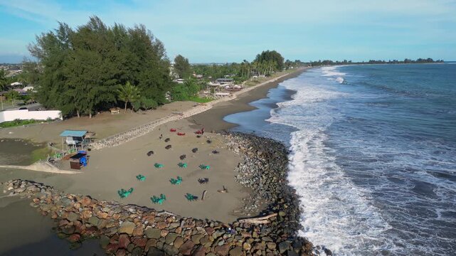 Meulaboh, Indonesia : Forward aerial drone footage of wave breaks into beach by small stalls in Meulaboh, coastal town in Aceh province of Sumatera in Indonesia.