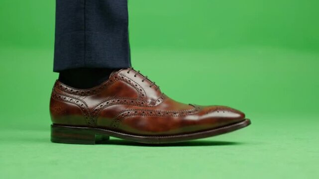 Brown leather oxford shoes walking on green screen, businessman in blue suit trousers walking in slow motion, close up of classic brogue leather footwear side profile, keyed background
