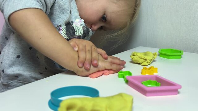 Child pressing pink modeling clay with hands at play table