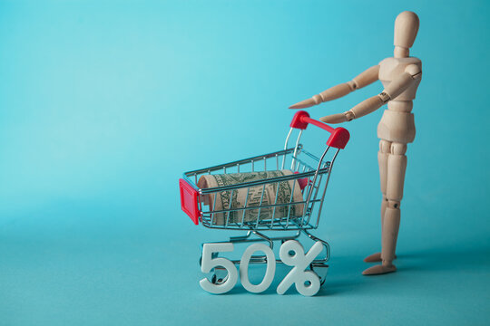 Wooden mannequin with shopping cart and 50 percent discount on blue background