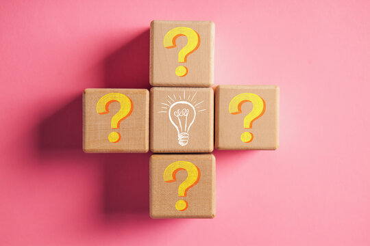 Question mark and light bulb on wooden cubes on pink background, top view