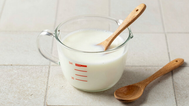 Glass measuring pitcher filled with milk and two wooden spoons on a tiled kitchen surface