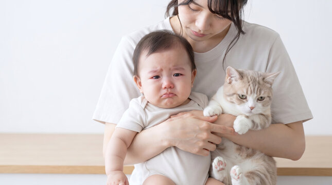 泣いている赤ちゃんと猫を優しく抱っこする母親