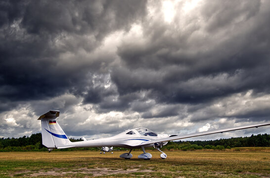 Motor glider parked on airfield runway with dramatic storm clouds gathering in the sky before takeoff