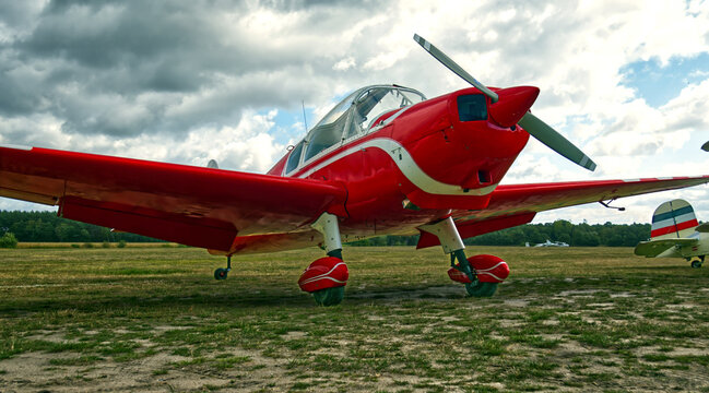Red vintage propeller airplane sitting on a grassy airfield under a cloudy sky, ready for flight and aviation
