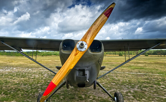 Vintage propeller aircraft parked on a grassy airfield, wooden propeller reflecting dramatic cloudy sky