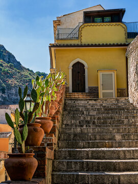 Vibrant Mediterranean travel photograph depicting a picturesque street and colorful historic houses beneath the mountains in Taormina, ideal for travel guides and lifestyle publications.