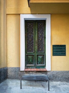 Green wooden door with wrought-iron ironwork, white stone frame, and yellow plaster wall in Taormina, Sicily, Italy.