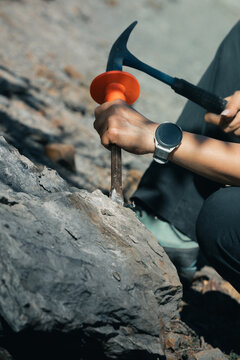 Close-up of a geologist or paleontologist using a rock hammer pick and chisel outdoor on rocky terrain to examine stones, mineral strata, and potential fossil formations.