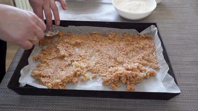 Woman spreading grated apple filling on baking sheet with spoon, Process of making homemade dessert putting apple filling on parchment pape