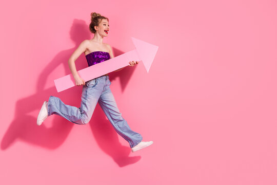 Young stylish woman holding large pink arrow prop on vibrant pink background celebrating fun and playful lifestyle