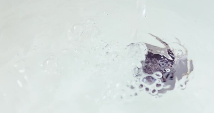 Clean running water flowing into a sink drain with bubbles and splashes, water use, drainage, hygiene, cleanliness and water conservation, close-up
