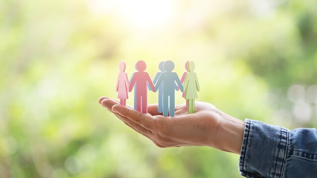 Hand holding colorful paper people figures against blurred green background, concept of community support, family care and diversity