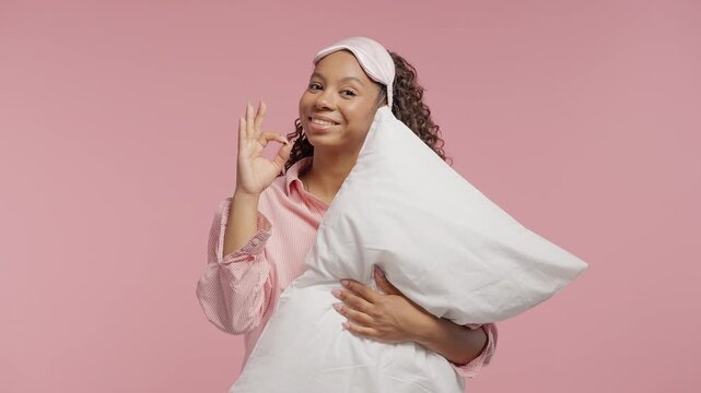 Young teen girl in pajamas holding soft pillow and showing ok okay hand sign. Relaxed morning portrait representing sleep, comfort, rest, home routine and cozy lifestyle.