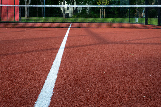 Empty Outdoor Tennis Court With Red Surface and Black Net