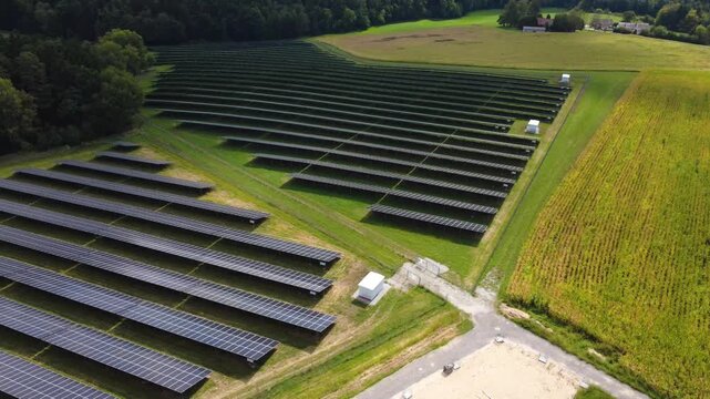 Low aerial flight along the edge of a solar farm with transformer stations and a cornfield