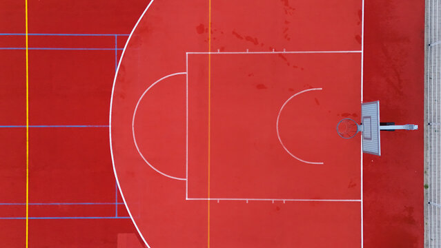 Aerial view of a vibrant red basketball court with white markings and a hoop in Riga, Latvia.