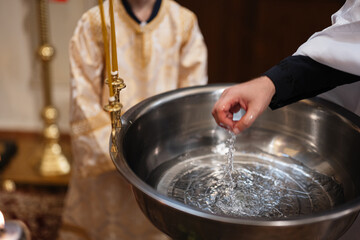Fototapeta premium Priest pouring holy water from a baptismal font during a child christening ceremony in church