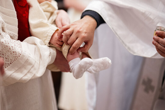 Priest baptizing a baby during a church christening ceremony as family holds the infant while oil is applied and prayers are said