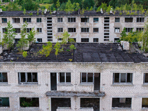 Aerial view of abandoned Soviet military buildings in Irbene, featuring derelict brick structures with trees growing on rooftops and through windows in Irbene, Ventspils Municipalit, Latvia.