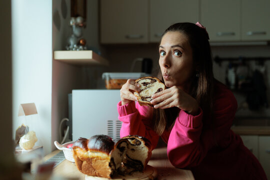 Surprised Woman Eating Traditional Sweet Walnut Bread In The Kitchen. Shocked lady consumes authentic sugary chocolate pastry inside her culinary room.