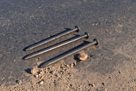 Three metal construction nails lying on asphalt road