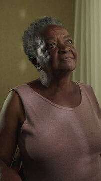 Wise senior African American matriarch gazing gently out residential windowpane embracing lifelong memories quiet gratitude and serene inner harmony