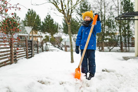 Young child helping shovel deep snow in a backyard on a sunny winter day. Playful outdoor household chore teaches responsibility and participation in family life.