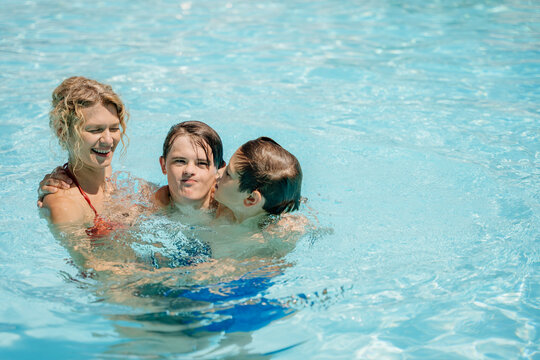Happy blonde mother with two sons enjoying close family moment in outdoor pool on summer day