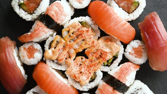 Assorted sushi platter slowly rotating to showcase colorful maki rolls, nigiri and fresh Japanese food arranged on a serving tray.