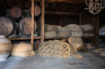 Dark cargo hold of a wooden ship stored with vintage wine barrels, hemp ropes, and supply sacks. © Adolf