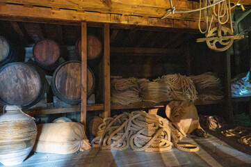 Dark cargo hold of a vintage wooden ship stored with wine barrels, hemp ropes, and supply sacks. © Adolf