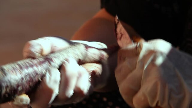 Gloved hands peeling purple black carrot with knife during traditional culinary preparation close up