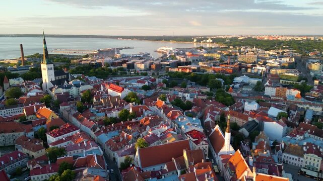 Aerial drone view over Tallinn Old Town with St Olaf Church rising among red rooftops. Tallinn Bay and the surrounding city extend toward the horizon in Estonia.