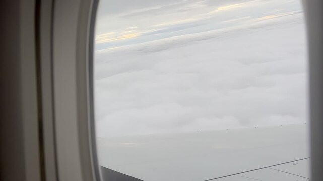 View from an airplane window showing part of the wing above a vast layer of white clouds. Bright sky and soft cloud formations create a peaceful scene over Russia