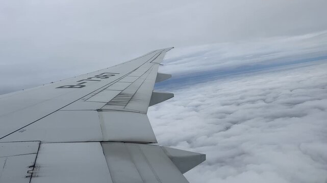 View from an airplane window showing the wing above a vast layer of white clouds. Bright overcast sky stretches across the horizon during flight over Russia.
