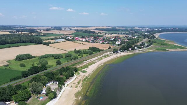 Aerial drone view showing Lake Wigry with sandy banks green trees and rural farmland. Villages and winding roads stretch across the countryside in Poland