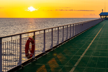 Stunning golden sunrise over the Baltic Sea viewed from a ferry deck. A peaceful marine landscape featuring a lifebuoy on the railing, ideal for cruise travel and vacation themes. © Vlad Rakin