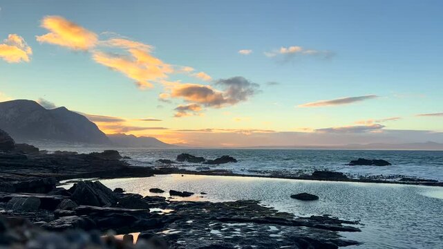 Timelapse. Vivid sunrise clouds fly over ocean viewed over Hermanus marine pool