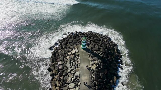 Aerial drone view following the path to a lighthouse in Viana do Castelo, Portugal, with powerful Atlantic waves breaking along the rocky coastline.