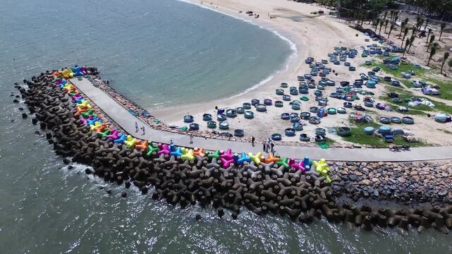 Drone video flying over vibrant colorful concrete wave breakers and sea defense structures with round vietnamese fishing boats along the coastline in Mui Ne, Binh Thuan province, Vietnam.