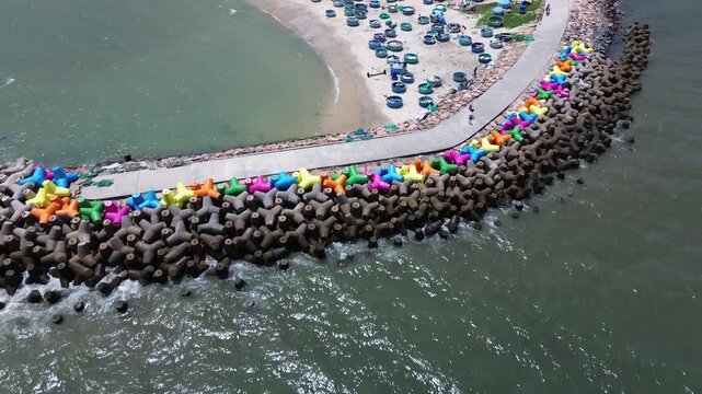 Drone video flying over vibrant colorful concrete wave breakers and sea defense structures with round vietnamese fishing boats along the coastline in Mui Ne, Binh Thuan province, Vietnam.