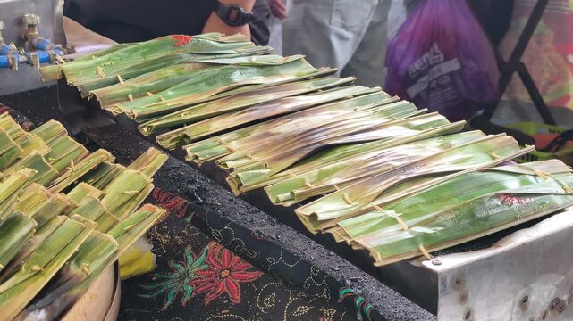 Traditional otak-otak is being cooked on a grill. It is carefully prepared and served hot for eager customers.