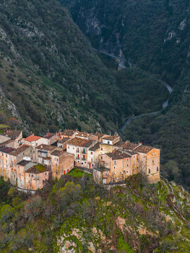 Aerial view of the historic stone houses of Anversa degli Abruzzi perched on a rocky cliff overlooking a deep valley with winding roads in Anversa degli Abruzzi, Abruzzo, Italy.