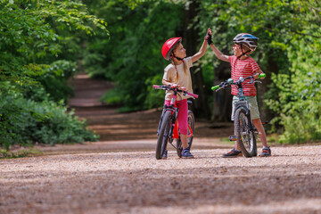 Fototapeta premium Children boy and girl high-fiving beside bicycles in the forest