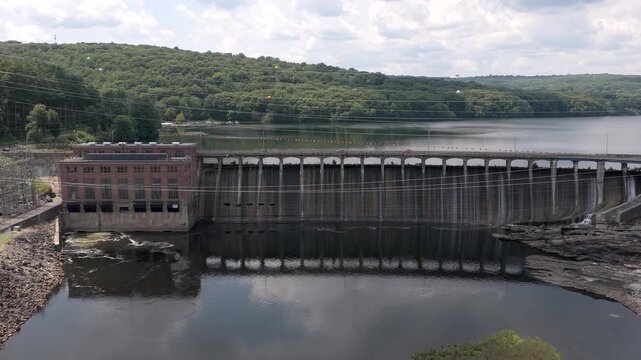 Water seeps down the face of Stevenson Dam on the Housatonic at Monroe, Connecticut, the brick powerhouse of the Stevenson Generating Station at one end and Lake Zoar behind. Aerial rising shot