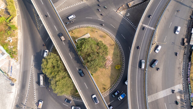 Aerial view of a highway interchange and roundabout with cars on asphalt roads, surrounded by green trees and urban infrastructure in Yogyakarta, Special Region of Yogyakarta, Indonesia.