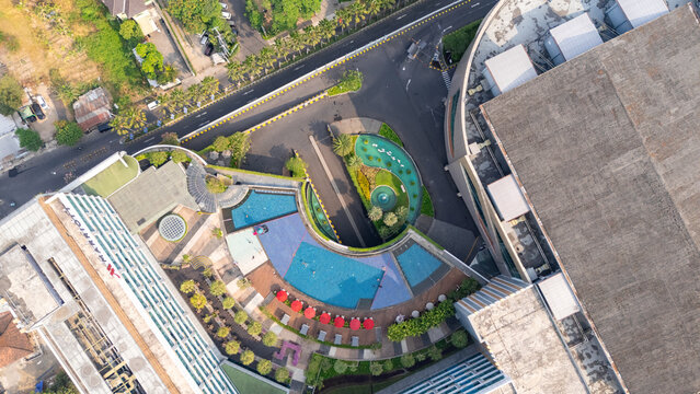 Aerial view of the Marriott Hotel featuring a curved swimming pool with red umbrellas, modern architecture, and surrounding urban landscape in Yogyakarta, Special Region of Yogyakarta, Indonesia.