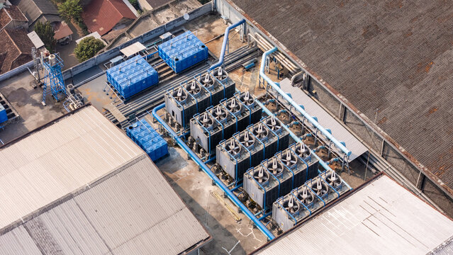 Aerial view of industrial cooling towers and blue water storage tanks on a factory rooftop in Yogyakarta, Special Region of Yog, Indonesia.
